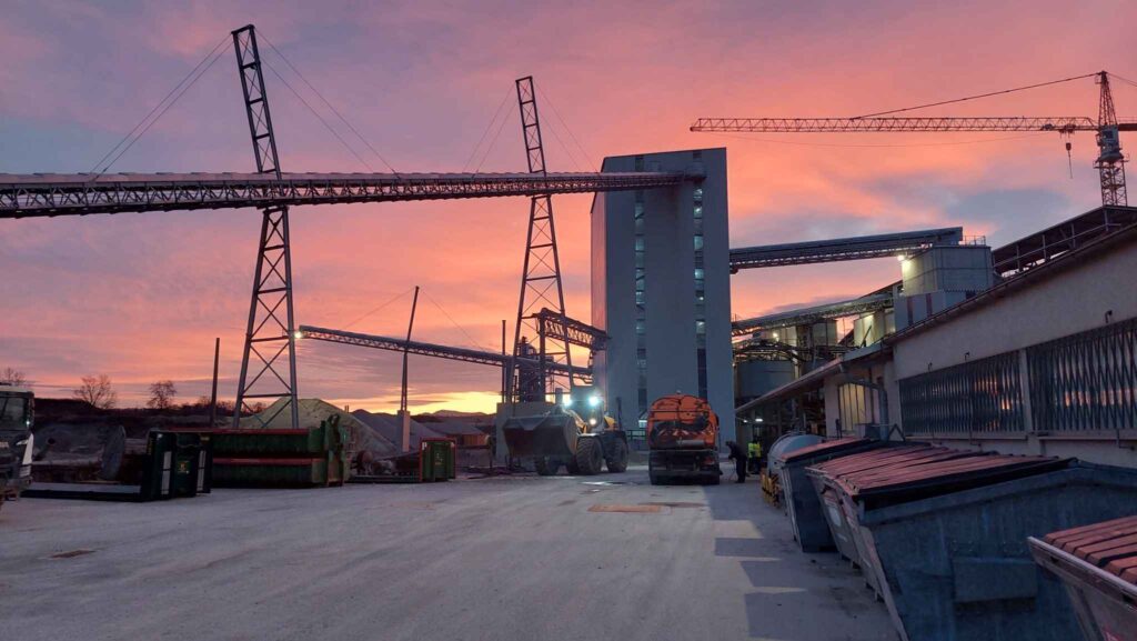 Industrielle Anlage bei Sonnenuntergang mit leuchtendem Himmel und schweren Maschinen im Vordergrund.